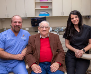 Smiling patient sitting with dentist and team member